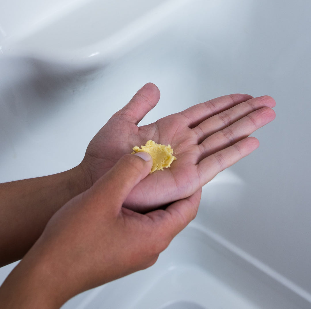 Person crushing dissolvable waterless conditioner tablet in their hands while in the shower.