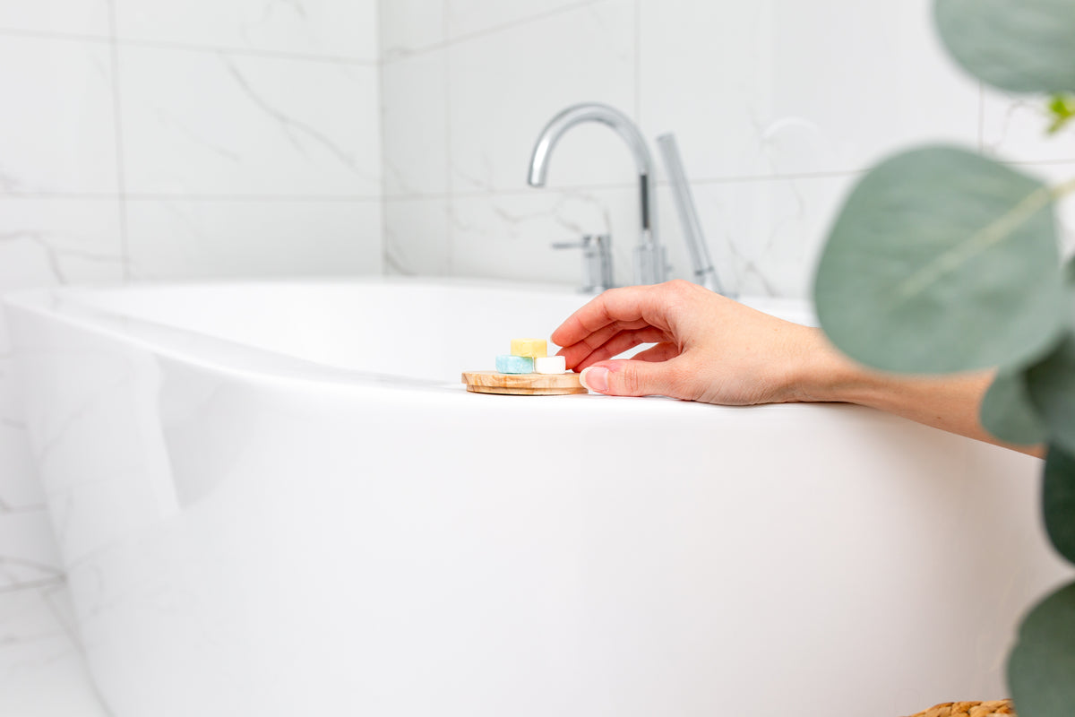 Image of hand reaching for pile of EarthSuds travel-size biodegradable soap tablets sitting on white bathtub