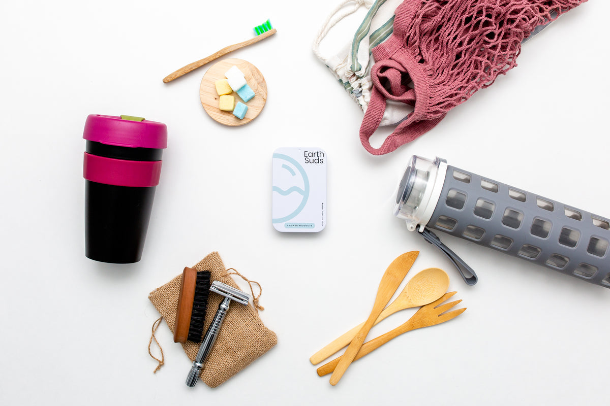 Image of plastic free personal items such as biodegradable cutlery, reusable water bottle, and EarthSuds travel shampoo and conditioner