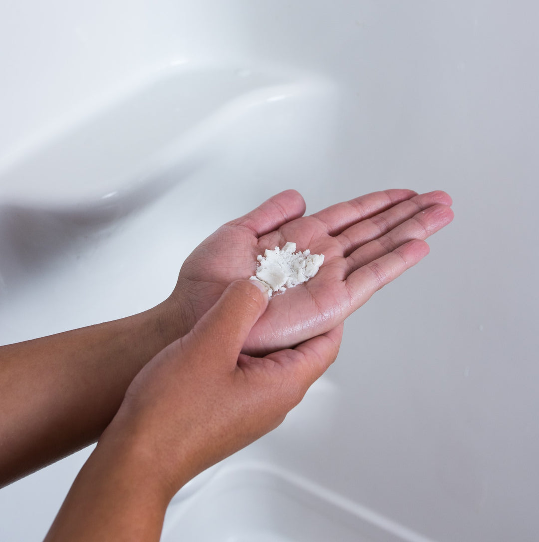 Person crushing dissolvable waterless shampoo tablet in their hands while in the shower.