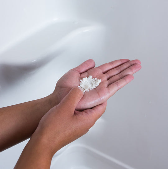 Woman crushing dissolvable waterless shampoo tablet in their hands while in the shower.